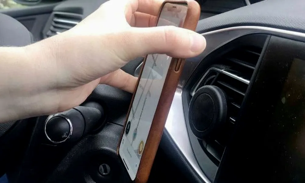 Conducteur voulant tester la compatibilité de son support de téléphone de voiture aimanté avec la coque de son appareil mobile